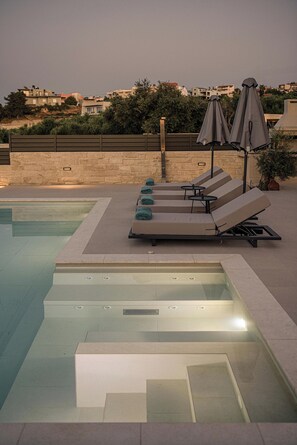 A rooftop pool area with lounge chairs and umbrellas, a clear pool, and a view of buildings in the background. - Kymélia Ground Suite With Private Pool & SeaView (Galatas)