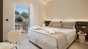 Habitación de hotel moderna con una cama grande, una silla, una mesita y un balcón con vistas a árboles.