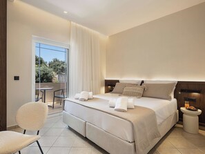 Habitación de hotel moderna con una cama grande, una silla, una mesita y un balcón con vistas a árboles.