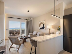 A modern kitchen with a central island, a dining area with wicker chairs, a sofa, and a view of the outdoors.