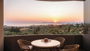 Un balcón con sillas de mimbre y una mesa, con vistas a un paisaje pintoresco al atardecer.