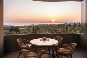 Un balcón con sillas de mimbre y una mesa, con vistas a un paisaje pintoresco al atardecer.