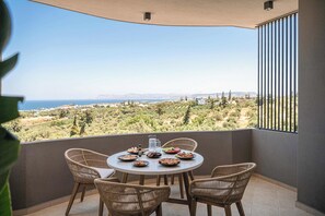 Un balcón con sillas de mimbre, una mesa redonda y vistas a un paisaje costero.