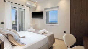 Un dormitorio con cama, una silla, un televisor y ventana con vistas.