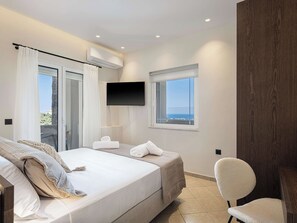 A bedroom with a bed, a chair, a TV, and a window with a view.