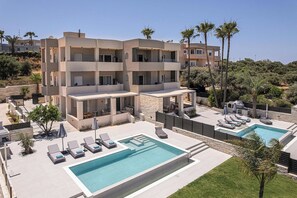 Un edificio moderno de varios pisos con piscina, tumbonas y un patio ajardinado.