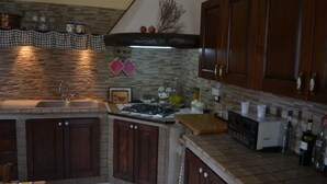 A kitchen with a stone backsplash, wooden cabinets, a gas stove, and a coffee maker. - Villa of Roses (Sicilia)