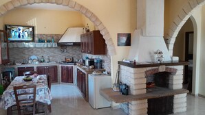 A kitchen with a stone archway, a built-in oven, and a dining area with a table set for two. - Villa of Roses (Sicilia)