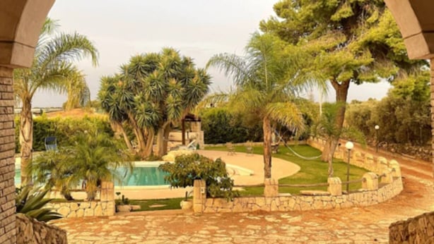A courtyard with stone flooring, palm trees, and a swimming pool. - Villa of Roses (Sicilia)
