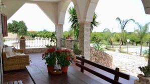 An outdoor patio with a wooden table and benches, surrounded by potted plants and a stone wall. - Villa of Roses (Sicilia)