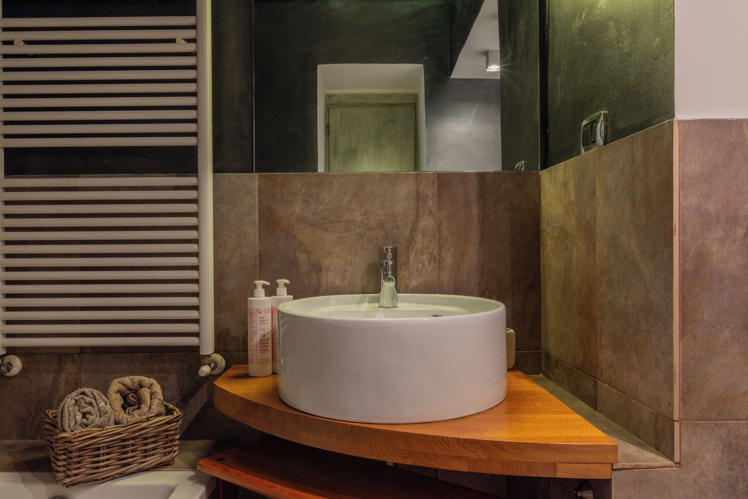 A bathroom with a round white sink, a wooden vanity, and a mirror above the sink.