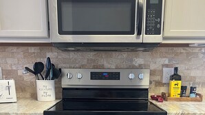 A kitchen with a stainless steel microwave, oven, and a digital clock displaying 12:54. - Beech Mountain Condo w/ spectacular views & close proximity to hiking and skiing (Beech Mountain)