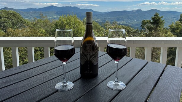 A wooden table with two wine glasses and a bottle of wine, set against a scenic mountain backdrop. - Beech Mountain Condo w/ spectacular views & close proximity to hiking and skiing (Beech Mountain)
