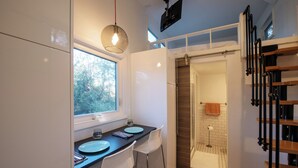 A compact kitchen with a dining area, a window, and a shower area with a towel rack.