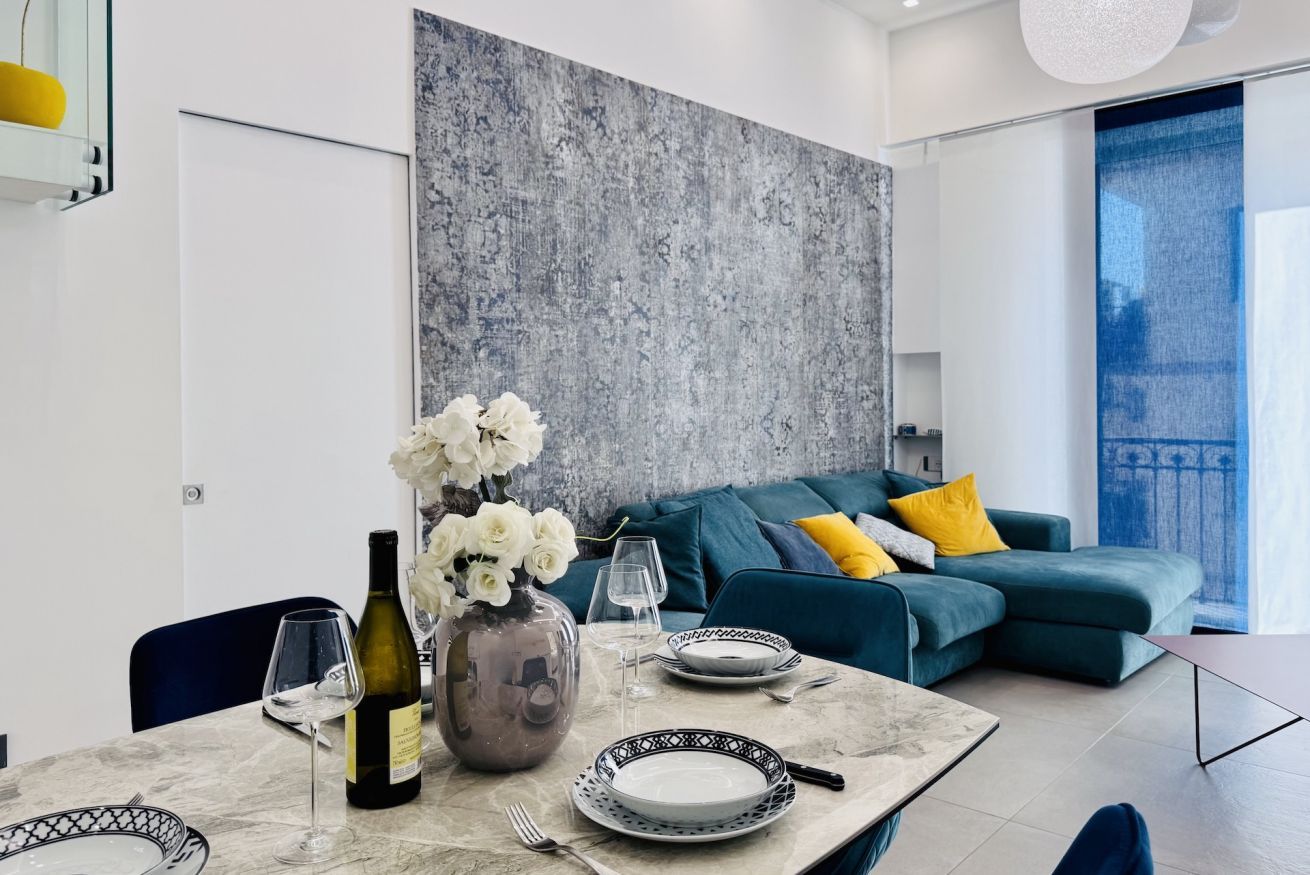 A modern living room with a sectional sofa, a dining table set with a vase of flowers, wine glasses, and plates.