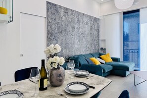 A modern living room with a sectional sofa, a dining table set with a vase of flowers, wine glasses, and plates.