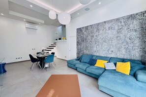 A modern living room with a blue sofa, a dining table, and a staircase leading to another level. - Ac Luxury Penthouse - private terrace (Meta)