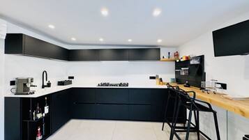A modern kitchen with black cabinets, a white countertop, a coffee machine, and a TV mounted on the wall.