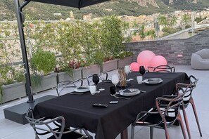 An outdoor dining area with a table set for four, surrounded by metal chairs, with a cityscape view in the background.