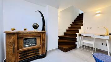 A staircase with wooden steps, a white wall, a wooden cabinet with a radio, and a white chair.