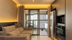 Una habitación de hotel moderna con sofá, una mesa de comedor y sillas, un ventanal corredero a un balcón y un horno empotrado.