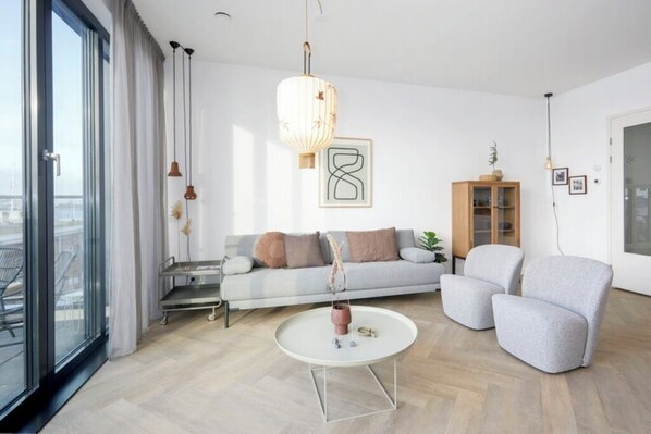 A modern living room with a sofa, armchairs, a coffee table, and a hanging light fixture.