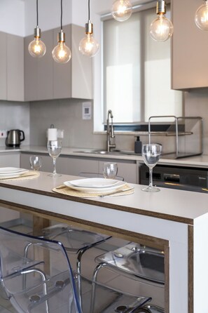 A modern kitchen with a central island, bar stools, and pendant lighting. - Beachcomber 2-BR Apartment in Larnaca (Larnaca)