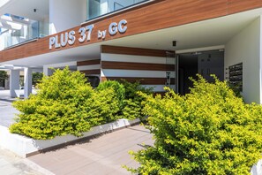 A hotel entrance with a sign reading 'PLUS 37 by GC' and a covered walkway with greenery. - Beachcomber 2-BR Apartment in Larnaca (Larnaca)