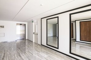 A modern hallway with a marble floor, a large mirror, and an elevator.