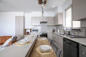 A modern kitchen with a dining area, equipped with stainless steel appliances, a dishwasher, and a coffee machine.