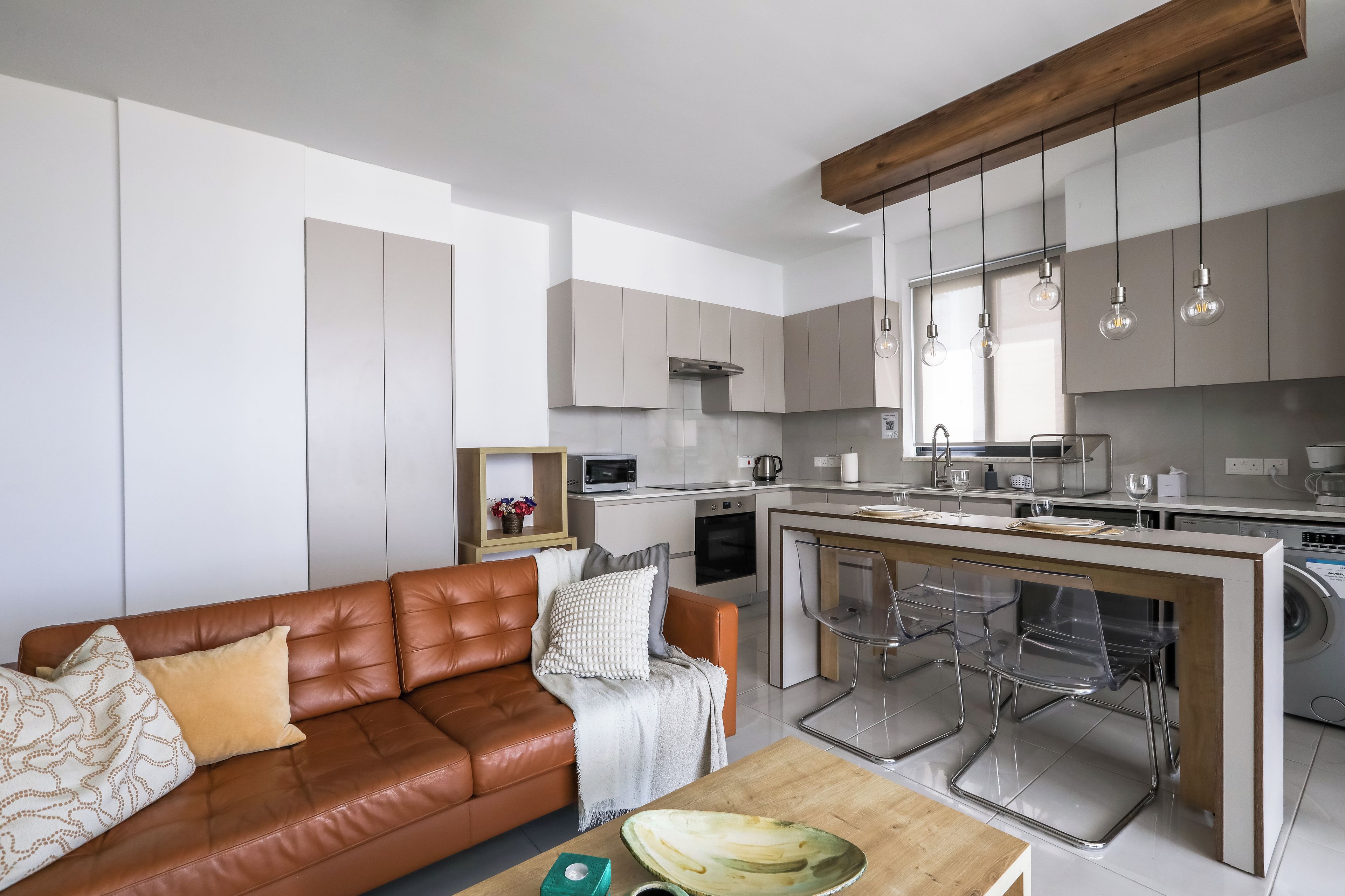 A modern kitchen with a central island, stainless steel appliances, and a dining area with clear chairs.