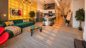 Uma sala de estar moderna com um sofá verde, uma mesa de centro de vidro e uma cadeira vermelha. Há uma área de cozinha com armários brancos e uma área de jantar com cadeiras verdes.
