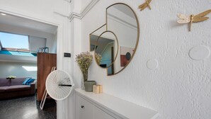 Een kamer met een wit aanrichtmeubel, een spiegel, een ventilator en een raam met uitzicht op een blauwe lucht.