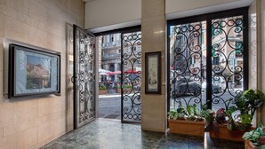 Een hotelentree met een marmeren vloer, metalen poorten, ingelijste kunstwerken en potplanten.