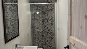 A bathroom with a wooden vanity, a toilet, a shower with floral wallpaper, and a green bath mat. - La Chintana (Ceres)