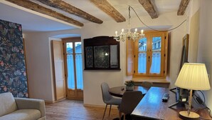 A living room with a sofa, a dining table with chairs, a chandelier, a lamp, and a large window with curtains. - La Chintana (Ceres)