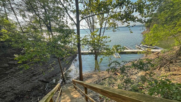 A wooden staircase leading to a dock by a calm lake, surrounded by trees and rocky terrain. - Blessing by the Lake | Lakeside Cabin|Hot Tub Wifi (Scottsville)