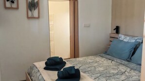 A neatly arranged bedroom with a bed, a bedside table, a hanging light fixture, and a door leading to another room. - STUDIO 263 "Studio with Provencal charm in Suze-la-Rousse - Calm & authenticity (Suze-la-Rousse)
