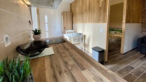 A modern kitchen with a wooden countertop, a built-in stove, and a ceiling vent. There is a dining area with a white table and chairs, and a small potted plant on the counter. - STUDIO 263 "Studio with Provencal charm in Suze-la-Rousse - Calm & authenticity (Suze-la-Rousse)