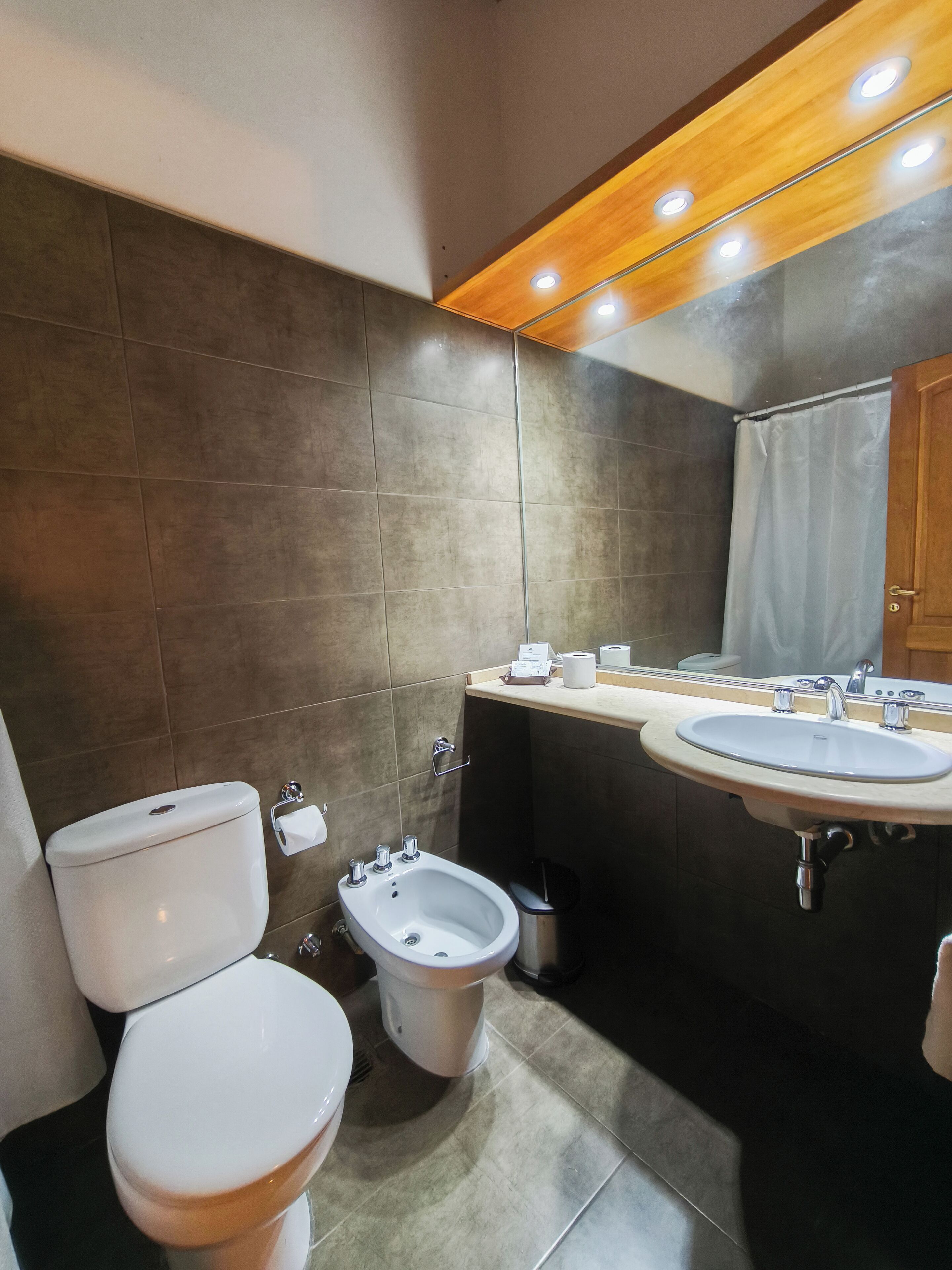 A modern bathroom with a toilet, bidet, sink, and mirror.