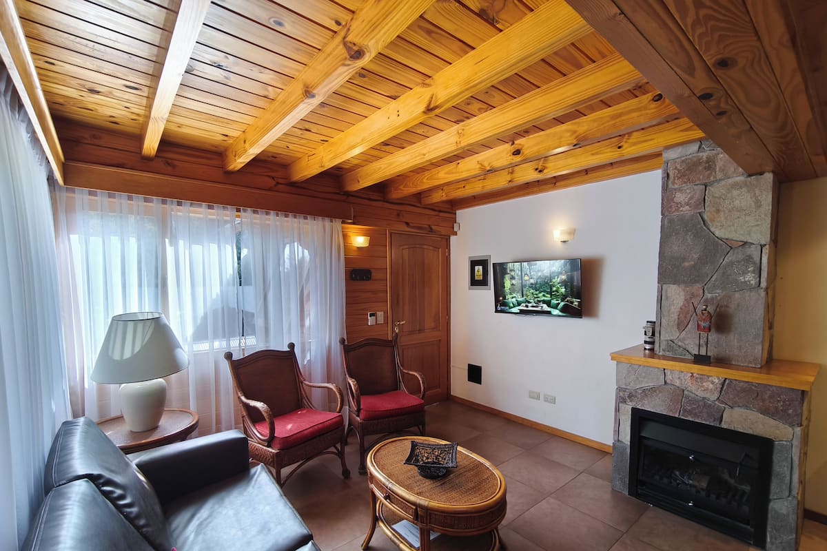 A cozy living room with a wooden ceiling, a stone fireplace, a television, and comfortable seating.