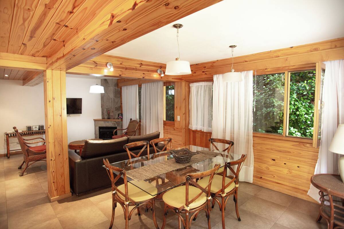 A wooden interior with a glass dining table surrounded by chairs, a sofa, and a fireplace.