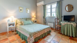 A bedroom with a bed, two bedside tables, a chair, a TV, a window with curtains, and an air conditioning unit. - Bed and Breakfast 'Provence' with Shared Terrace, Shared Garden and Wi-Fi (Estézargues)