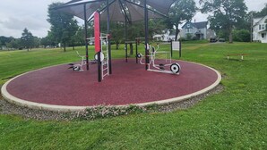 Ein Spielplatz mit Spielgeräten, einem überdachten Bereich und einer roten, gummierten Oberfläche.