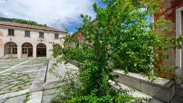 A courtyard with a building featuring arched doorways and a tiled roof, surrounded by greenery.