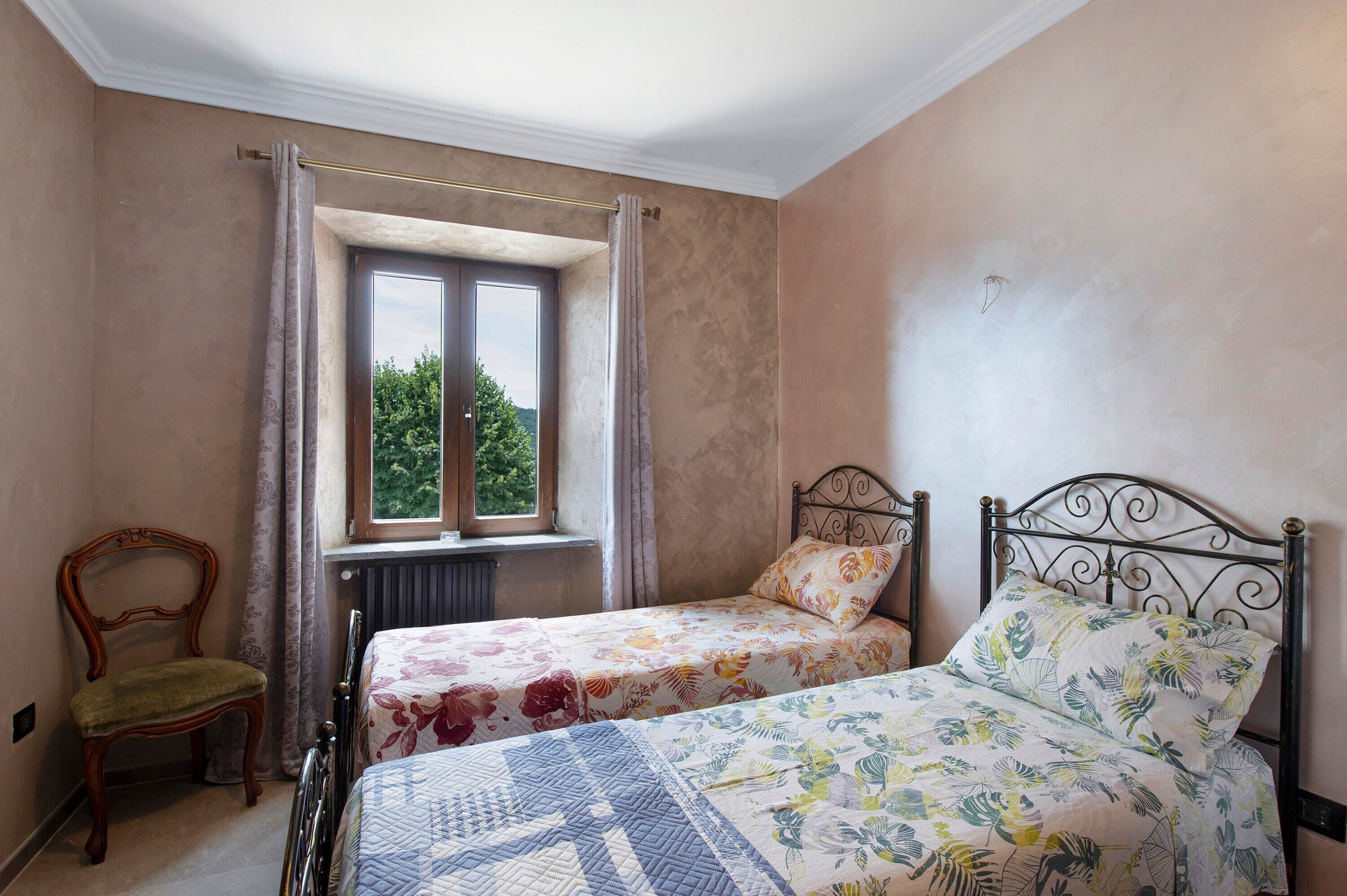 A bedroom with two single beds, a chair, a window with curtains, and a radiator.