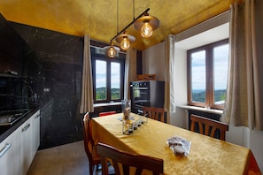 A dining area with a table set for two, a kitchen with a black marble backsplash, and a view of the landscape through the windows. - Apartment in a Villa (Mosso Santa Maria)