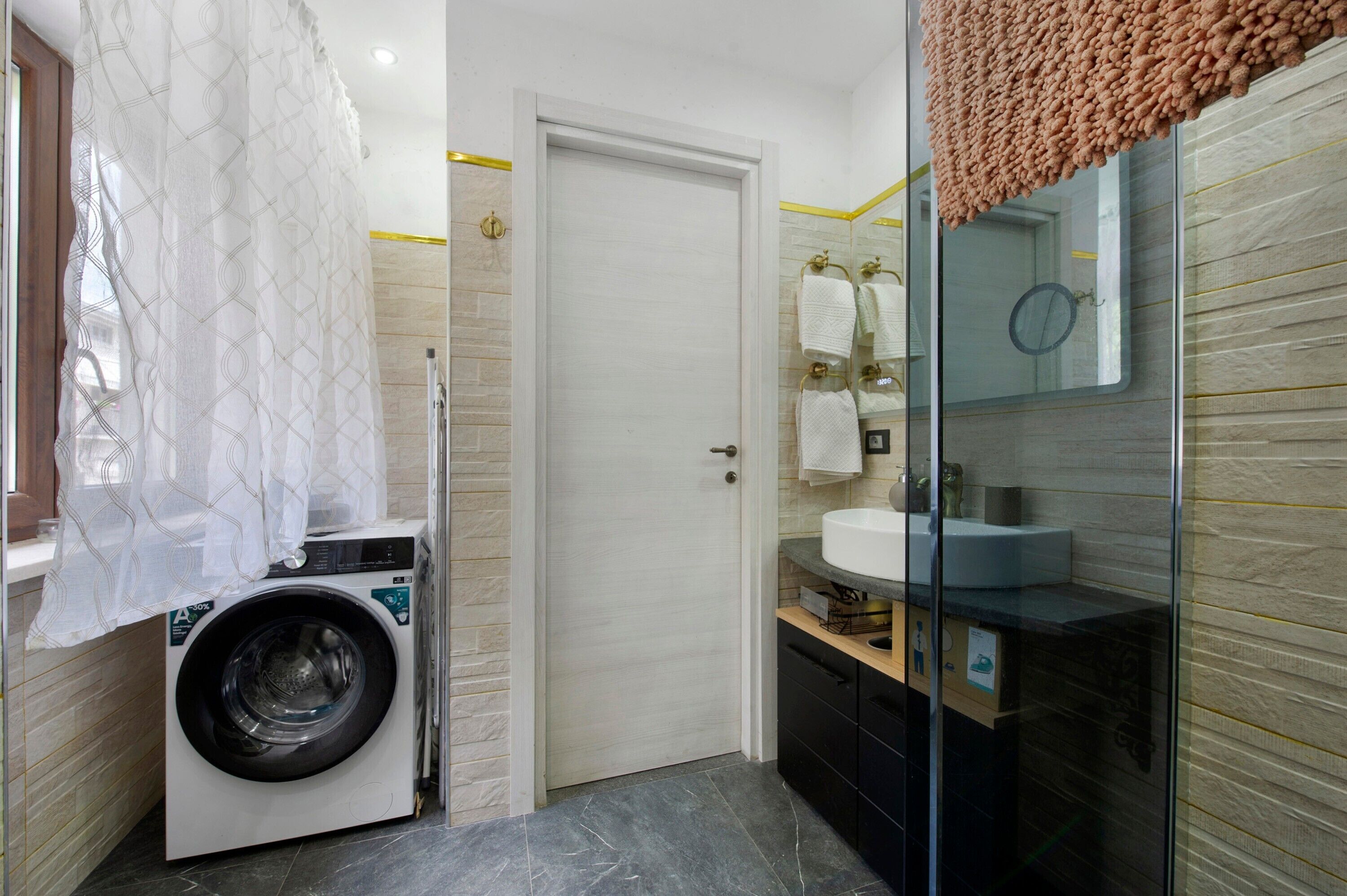 A compact bathroom with a washing machine, a glass shower enclosure, and a sink with a mirror.
