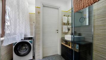A compact bathroom with a washing machine, a glass shower enclosure, and a sink with a mirror.