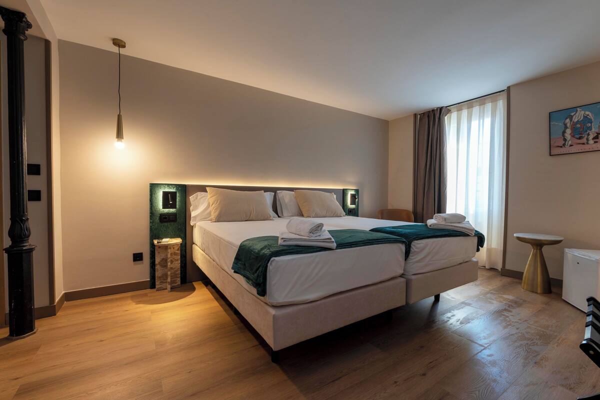 A hotel room with a large bed, a bedside table, a small table, and a painting on the wall.